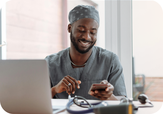A man smiling at his desk as he reads a text message on his phone.