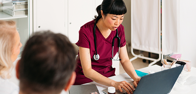A woman typing on her laptop while two people chat with her.